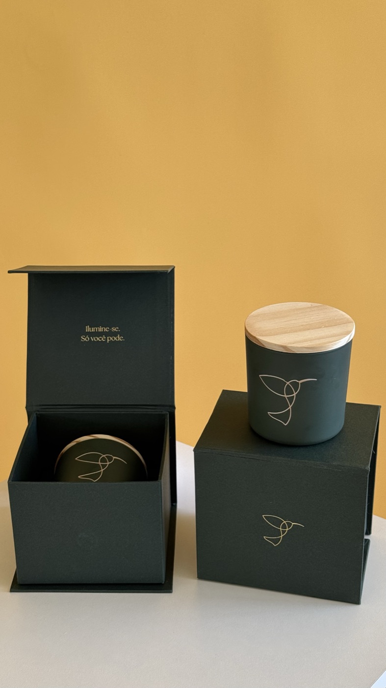 Vela aromática Casa Almes com tampa de madeira e caixa verde com o beija-flor dourado